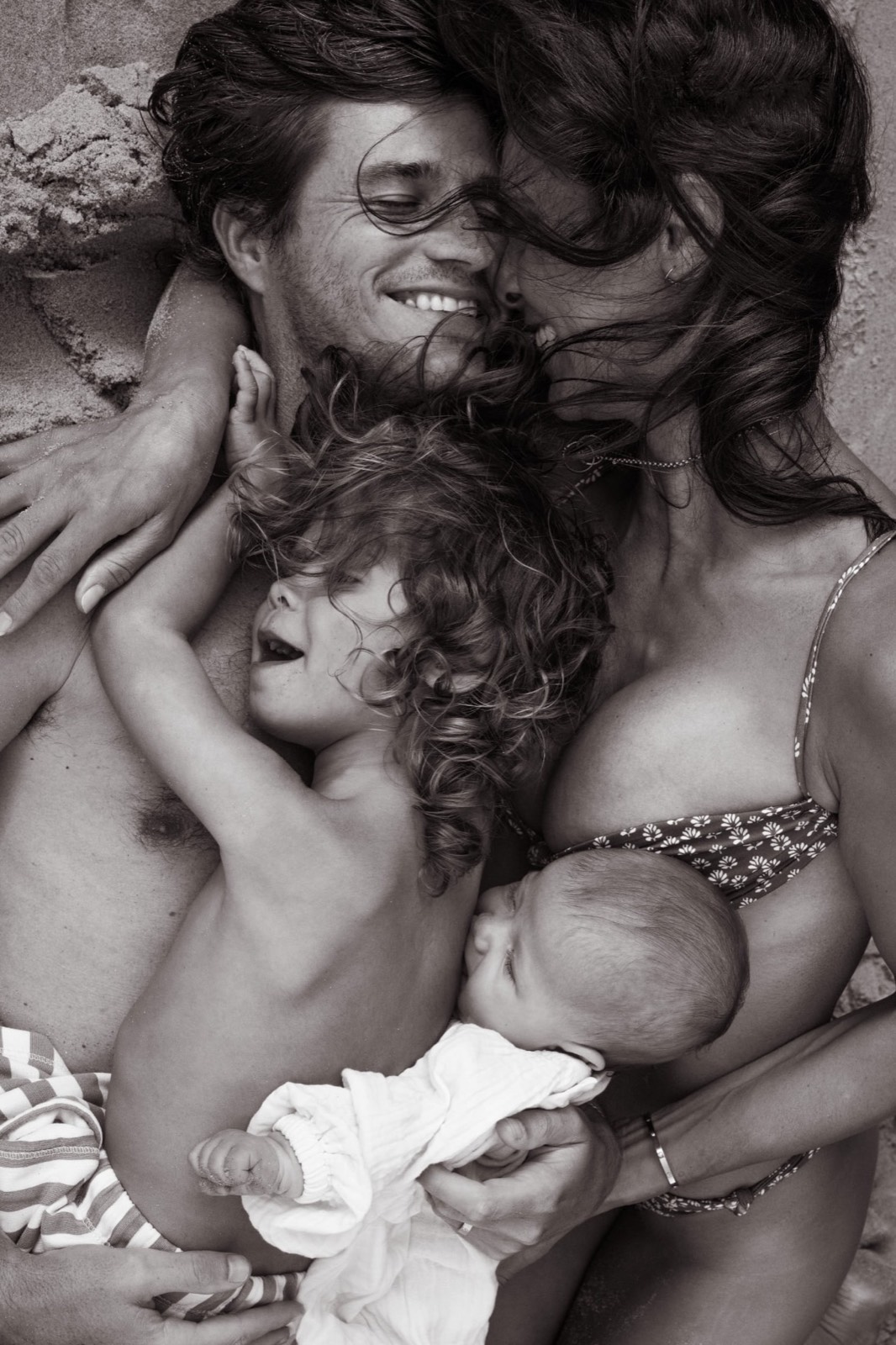 Intimate black-and-white family portrait of parents and children together on the sand
