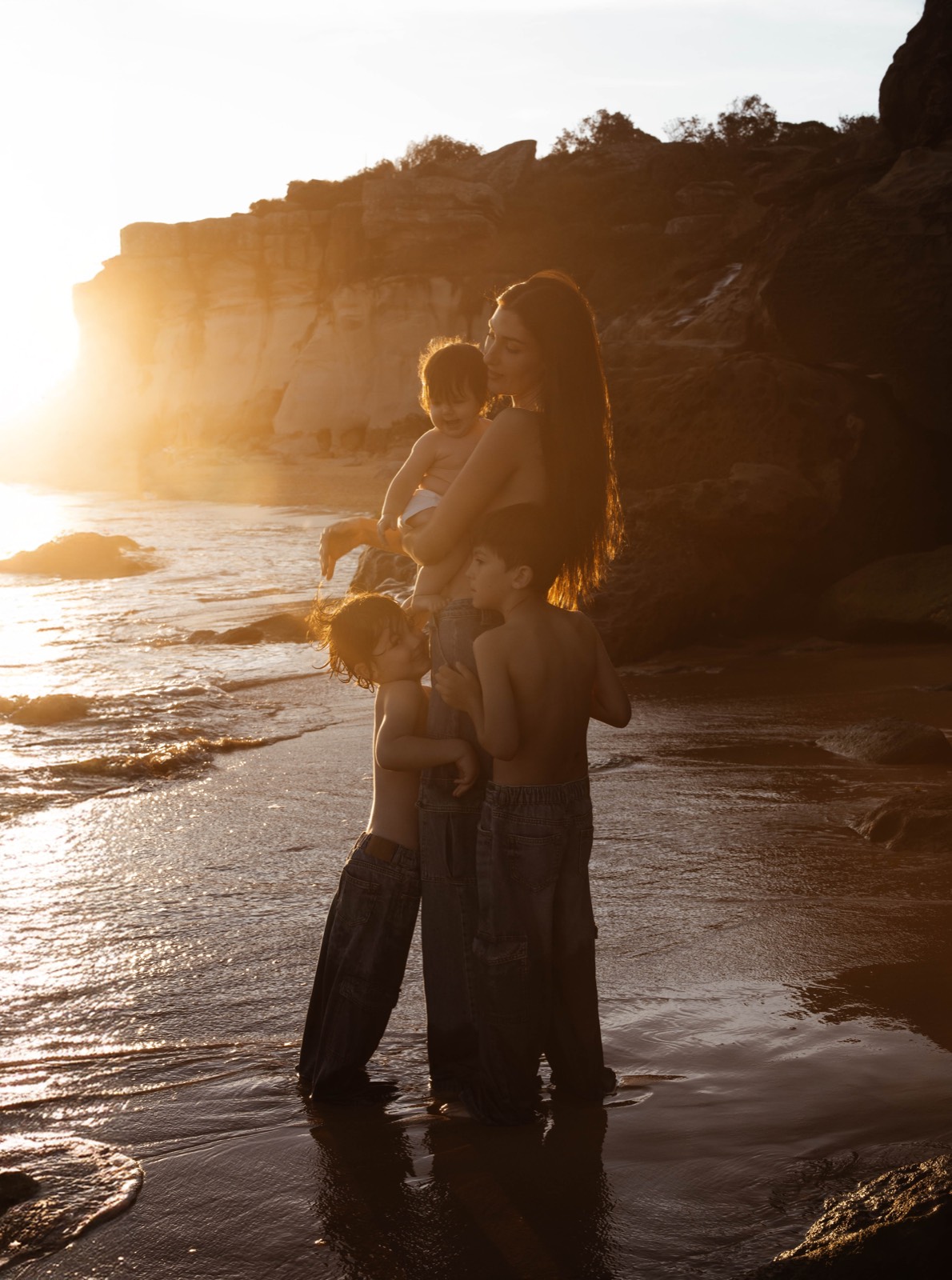 Mother holding her baby as her children gather around her at sunset