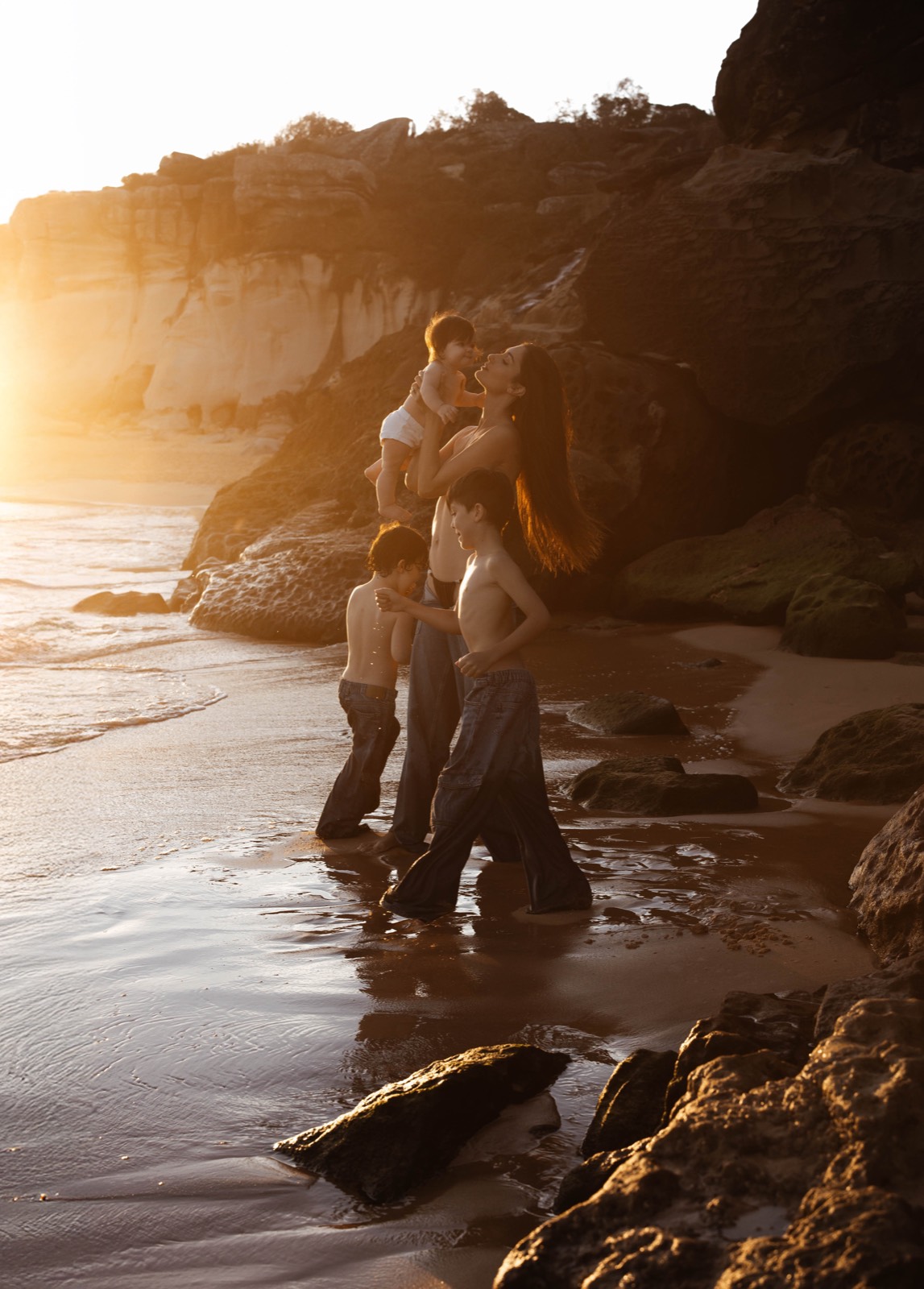 Mother lifting her baby as her children move along the shoreline
