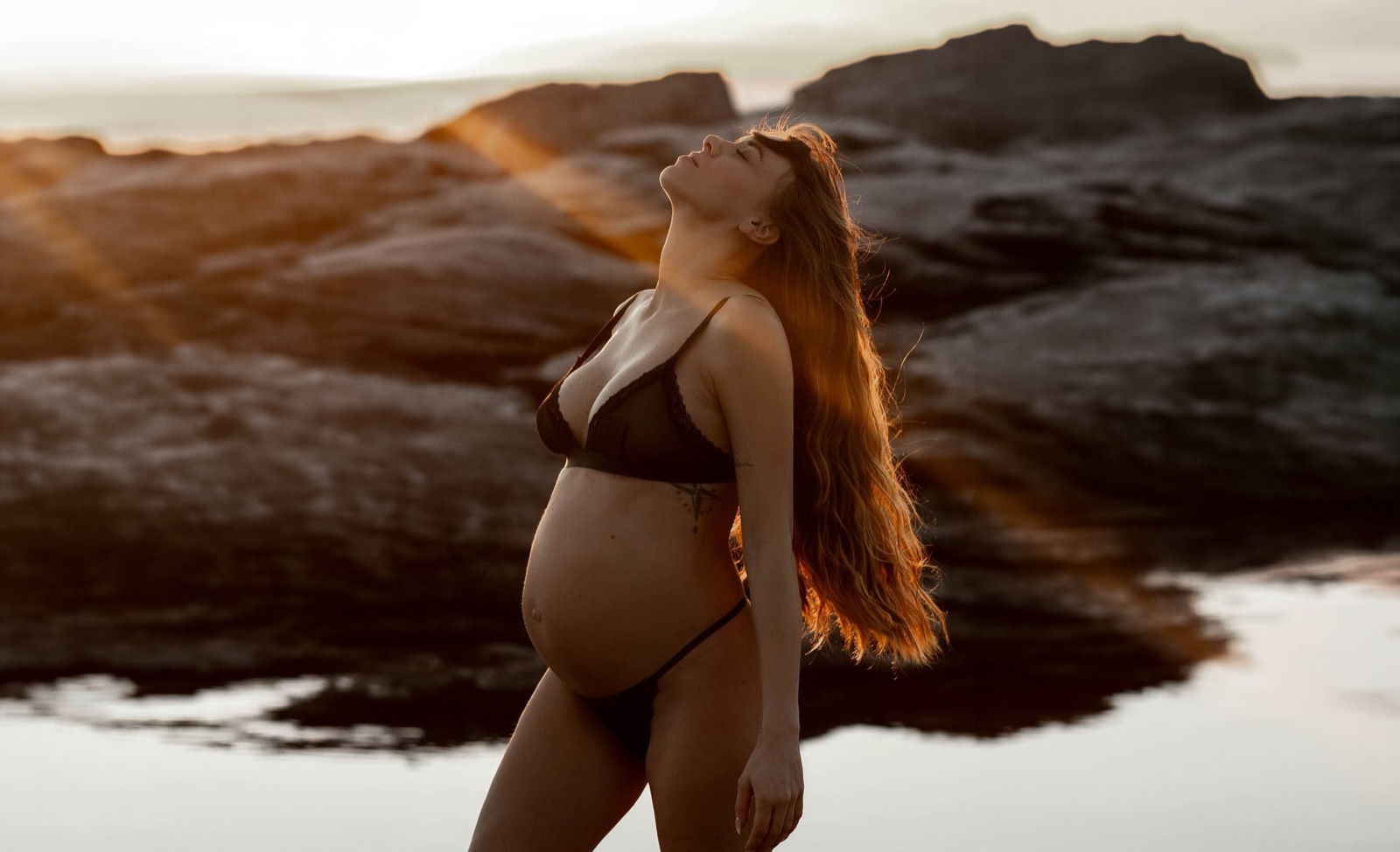 Pregnant woman standing in glowing panoramic coastal light